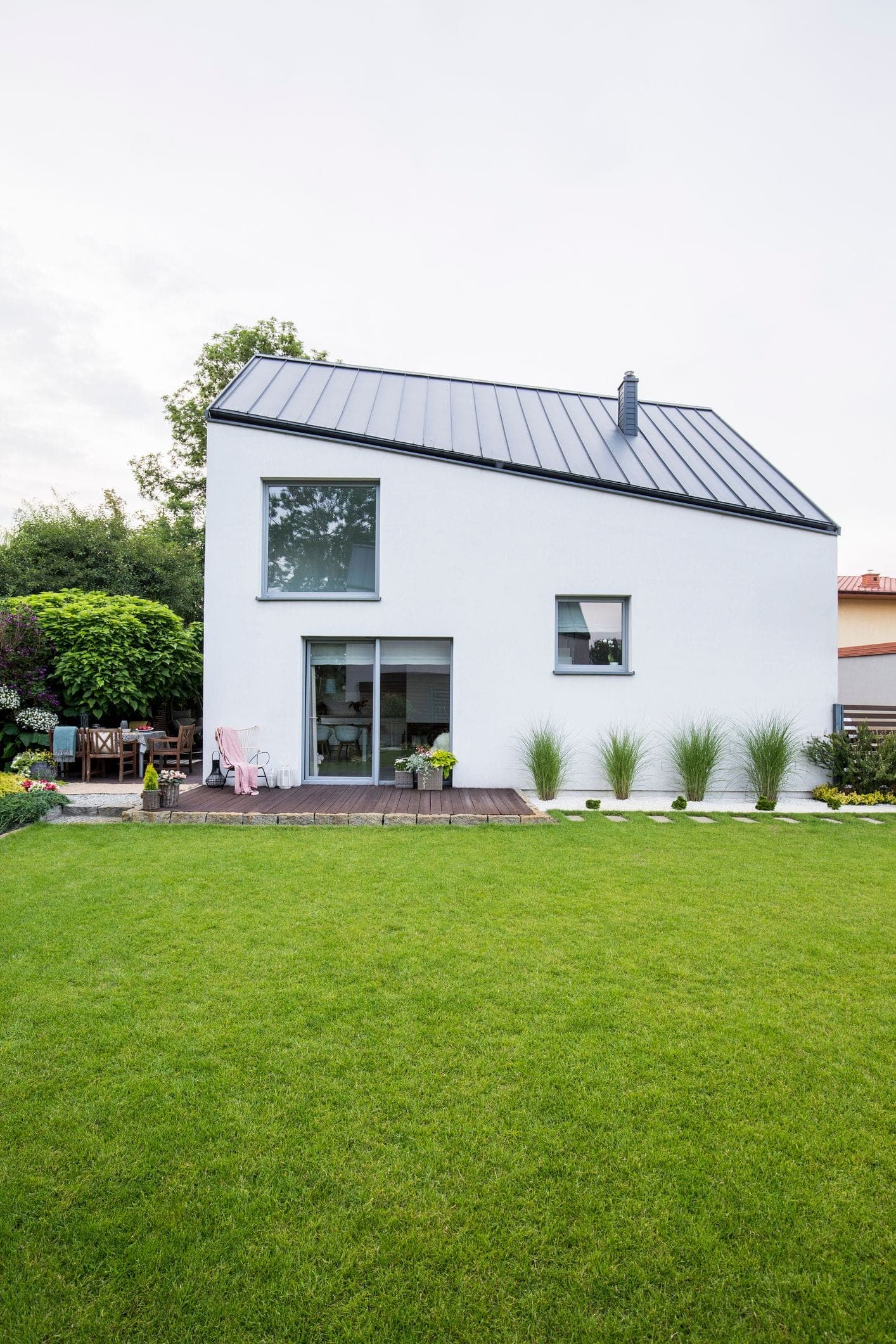 Zadní pohled na moderní rodinný dům s terasou a velkými okny, obklopený udržovanou zahradou.
