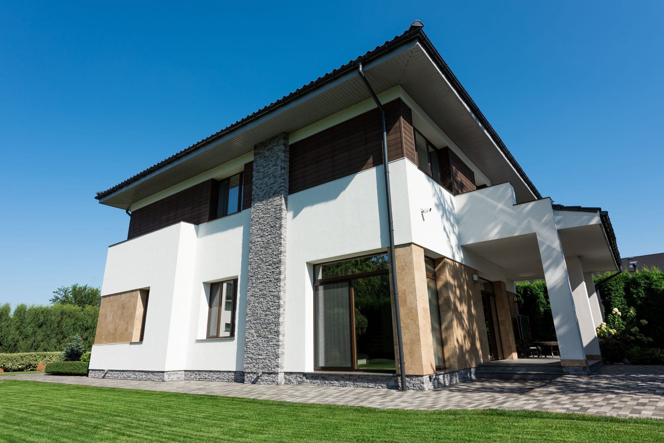 Moderní rodinný dům s elegantní fasádou v bílé barvě, kombinací kamene a dřeva, s prostornou terasou a udržovanou zahradou.